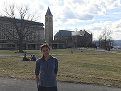 A photograph of Cornell Engineering student Sydney standing on the Arts Quad with the Clock Tower in the background