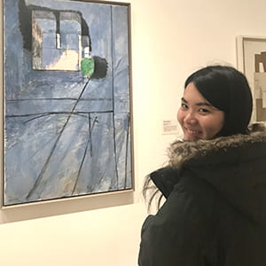 A photograph of Cornell ENgineering student Reina in front of a painting