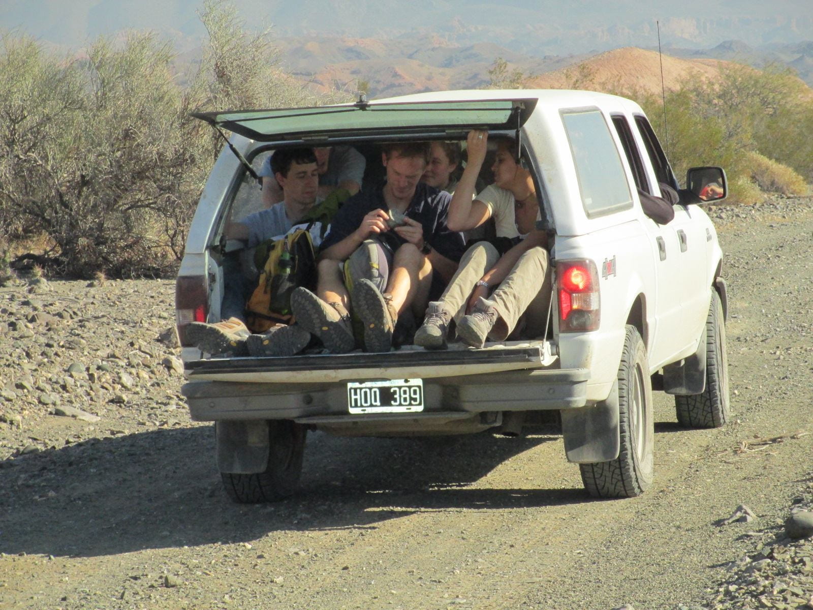Undergraduate students crammed into the back of an SUV with the back hatch open on rugged, mountainous terrain. 